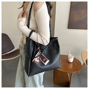 Side view of a large black leather tote bag with woven straps and decorative silk scarf