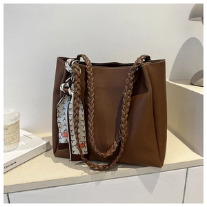 Detail of a large brown tote bag with woven handles and a decorative silk scarf accessory