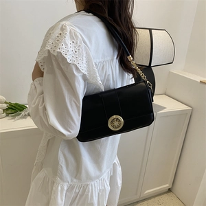 Elegant black chain crossbody bag with gold buckle shown on a model in a minimalist setting