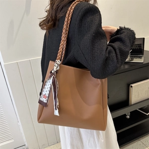 Brown leather tote bag with woven handles and decorative scarf in a lifestyle setting