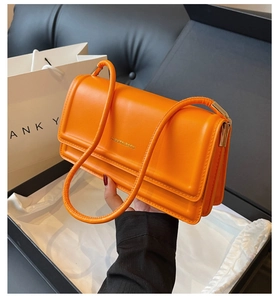 Detail of bright orange shoulder bag showing gold fashion lettering and double straps