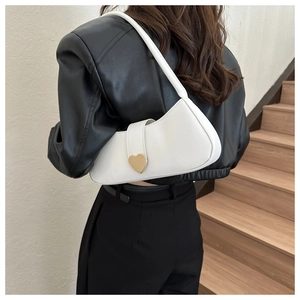 Close-up of a white crescent underarm bag featuring a large golden heart metal buckle