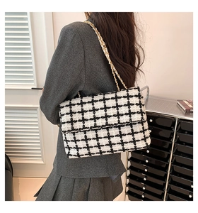 Détail du sac à carreaux en tweed avec chaîne dorée porté par un mannequin en costume gris