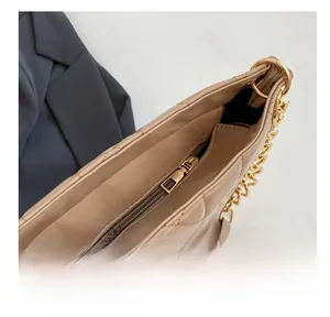 Detailed close-up of a cream quilted tote bag showing the smooth golden zipper and metal chain