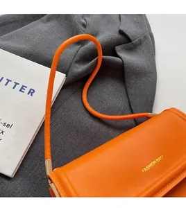 Detailed close-up of a bright orange underarm bag with gold FASHION BAGS text