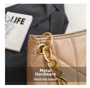 Close-up of golden metal chain and quilted texture on a beige shoulder bag