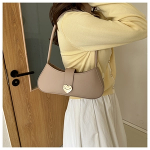 Detail of minimalist khaki shoulder bag with gold heart buckle worn by a model