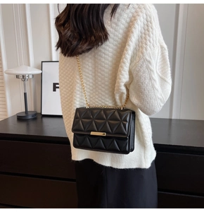 Detail of glossy black quilted shoulder bag featuring gold chain and metallic clasp