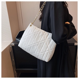 Detail of white quilted tote bag with gold chain strap on black dress model