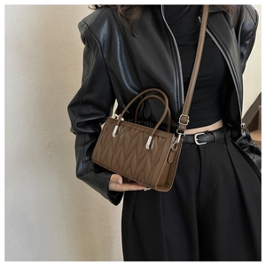 Detail view of brown quilted handbag with vertical pleats and silver-tone hardware