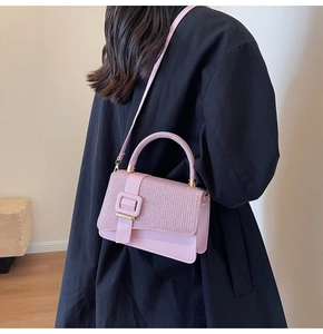 Detail of pink crossbody bag with woven texture and gold-tone buckle on black coat