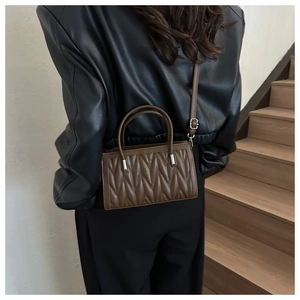 Detail of brown quilted faux leather handbag with vertical stitching and top handle