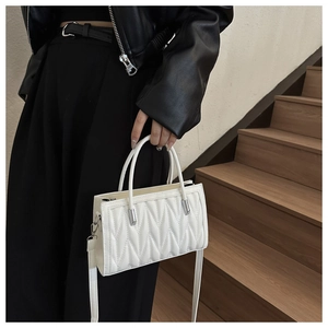 Detail of white wave-quilted handbag with dual handles and adjustable shoulder strap
