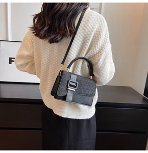 Detail of black glitter flap and leather crossbody bag on white waffle sweater