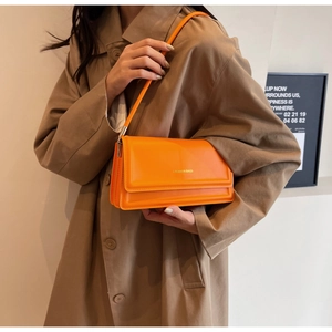 Detailed close-up of a bright orange leather underarm bag featuring gold lettering