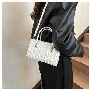 Close-up of a white quilted crossbody handbag worn on the shoulder in a minimalist setting