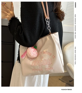Detail of off-white tote bag featuring pink embroidery, chain strap and peach pendant