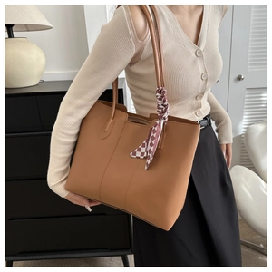Caramel brown tote bag with decorative plaid scarf shown in a lifestyle street fashion view