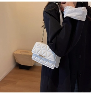 Detail of white quilted crossbody bag with gold chain strap and metallic hardware accents