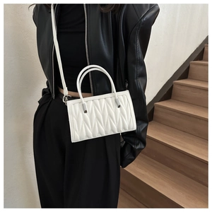 Close-up of white quilted handbag featuring vertical pleats and round top handles