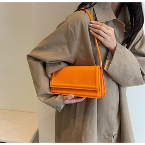Detail of orange geometric shoulder bag with embossed texture and gold lettering