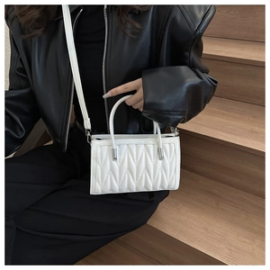 Detailed view of white quilted crossbody bag with V-shaped stitching on wooden stairs