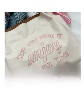 Detail of off-white tote bag with pink summer embroidery and strawberry charm
