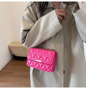Detail of rose pink quilted crossbody bag with gold chain strap and metal clasp on coat