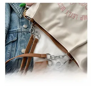 Detail of silver chain link connecting brown leather strap to the beige tote bag