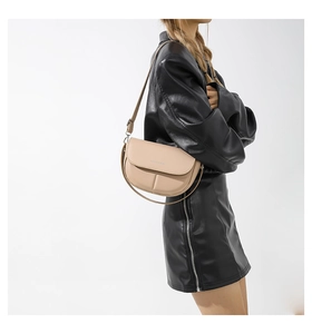Dettaglio della borsa a sella beige a semicerchio con linee sbalzate e logo in metallo