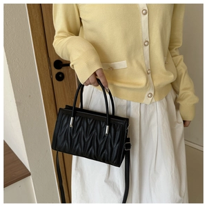 Detail of black quilted leather handbag with dual handles and adjustable strap on model