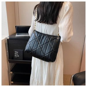 Detail of black quilted shoulder bag with geometric stitching and gold chain strap