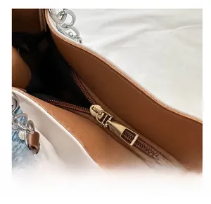 Detail view of smooth golden metal zipper and brown lining on a beige tote bag