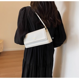 Detailed view of the white leather shoulder bag with gold lettering on a soft cream background