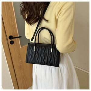 Detail of black quilted leather handbag with V-shaped texture on a model shoulder