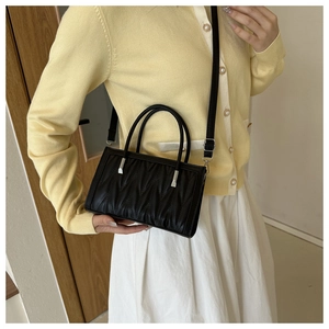 Close-up of black PU leather handbag featuring quilted wave patterns and silver hardware