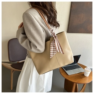 Beige tote bag with brown straps and plaid scarf shown on a model in a cozy office setting