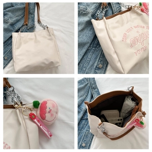 Detail view of off-white tote bag with enjoy embroidery and peach plush charm accessory