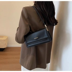 Close-up of black leather shoulder bag with gold metal buckle shown on a model