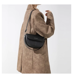 Dettaglio di una borsa a sella in pelle nera con patta elegante e scritte bianche di moda