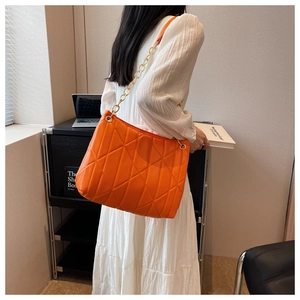 Detail view of orange quilted shoulder bag with golden chain strap on a model