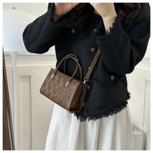 Brown quilted crossbody bag with circular handles and detachable strap shown on a model