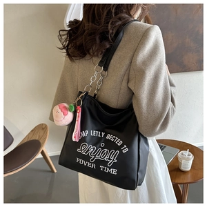Close-up of black tote bag featuring white embroidery and metallic chain strap detail