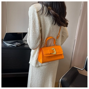 Detail of orange crocodile embossed handbag with baroque golden buckle worn by a model