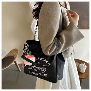 Close-up of black tote bag with white lettering and a cute pink plush charm accessory