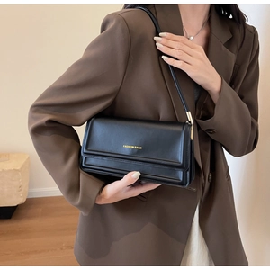 Close-up of black leather shoulder bag with fashion bags gold lettering on brown blazer