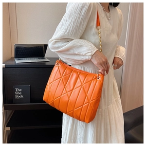 Detail of vibrant orange quilted shoulder bag with gold chain and plush triangular pattern