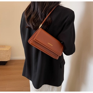 Brown leather rectangular shoulder bag with golden text shown on a model in a blazer