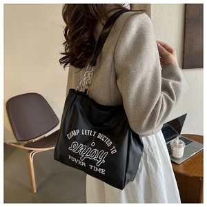 Close-up of black leather tote bag with silver chain details and white text embroidery