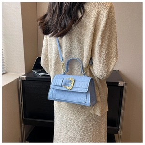 Detail of light blue crocodile embossed handbag with ornate golden buckle worn by model